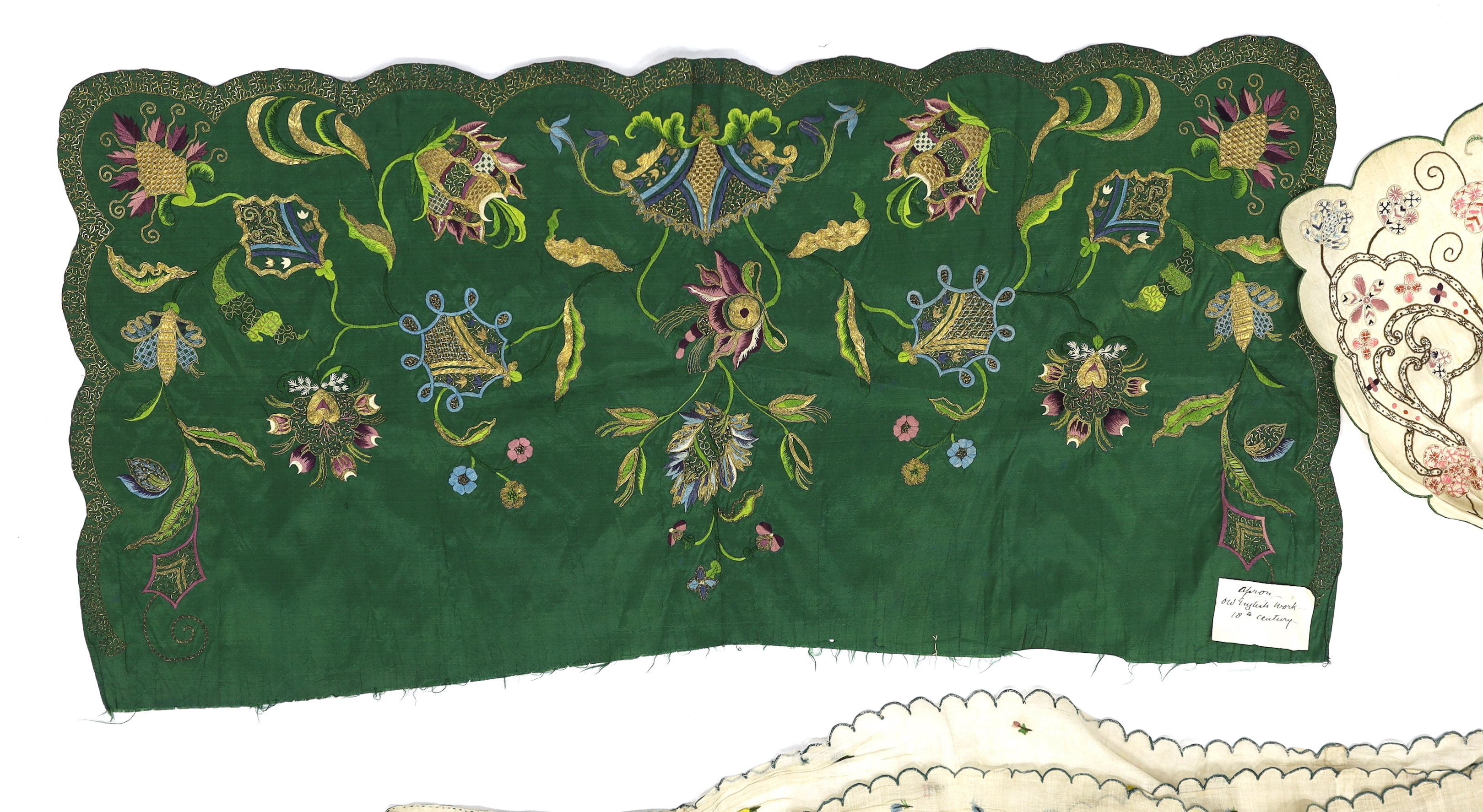 A late 18th century green silk scalloped bordered lady’s apron border, ornately embroidered with gold metallic threads and polychrome silk, in a large vine, floral and leaf design, together with a similar cream silk embr
